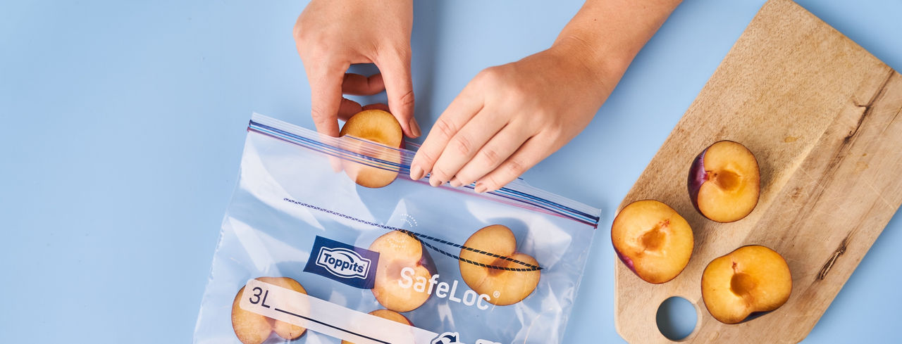 Halbierte Pflaumen werden in einen Toppits SafeLoc Beutel auf Holzbrett gelegt und verschlossen.