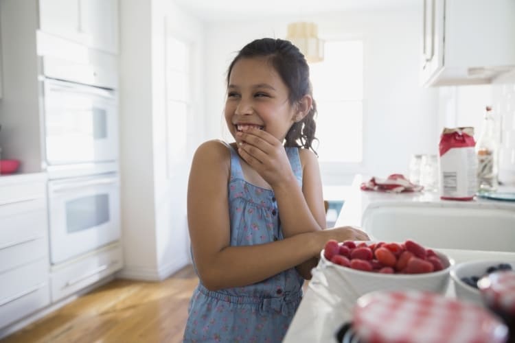 Jeune fille dans sa cuisine avec un bol de framboises et un film fraîcheur.