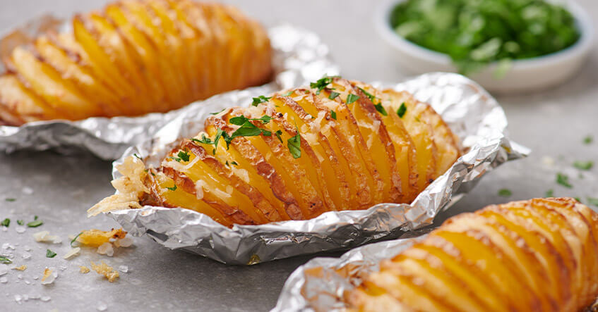 Pommes de terre Hasselback dans des papillotes en aluminium avec du fromage et des fines herbes