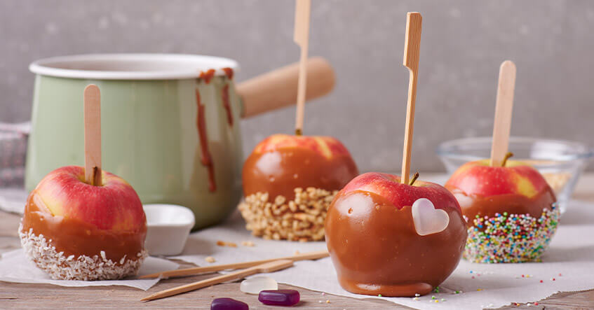 Pommes d’amour au caramel décorées d’éclats de noisettes, de noix de coco râpée et de perles de sucre