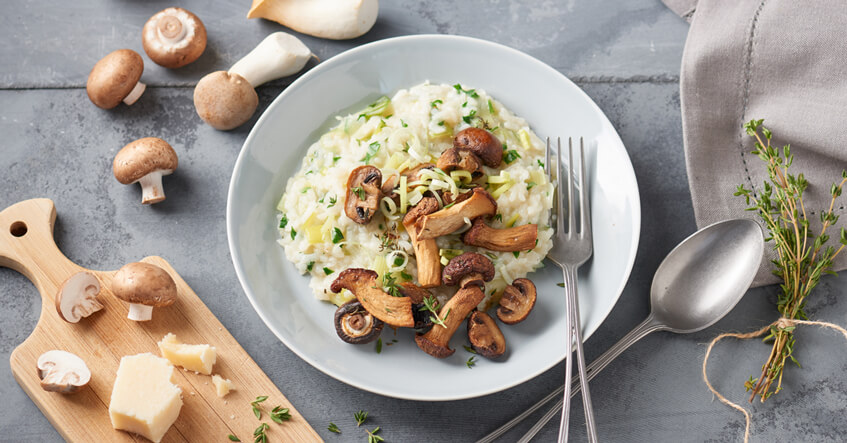 Pilzrisotto auf einem Teller mit frischen Pilzen drumherum